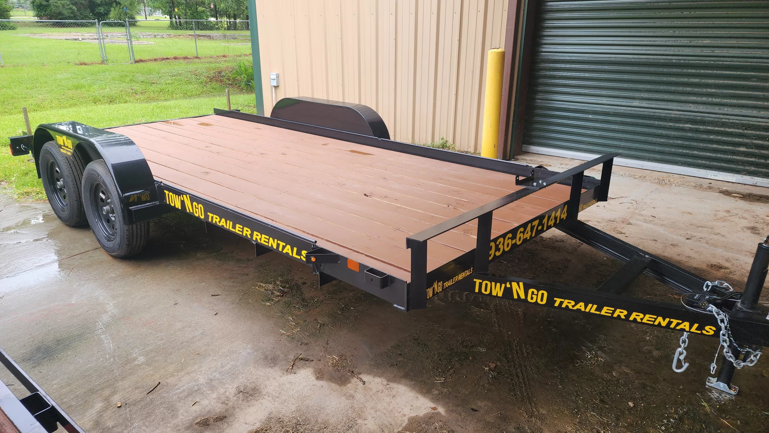 A 16-foot tandem-axle car hauler trailer with a flat wood deck, low-profile slide-out ramps, and heavy-duty D-ring tie-down points.